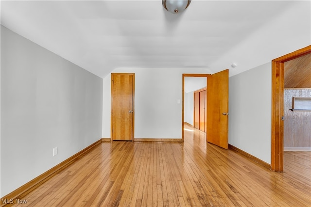 spare room with light wood-type flooring and vaulted ceiling