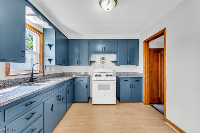 kitchen with light hardwood / wood-style floors, light stone counters, blue cabinetry, white range, and sink