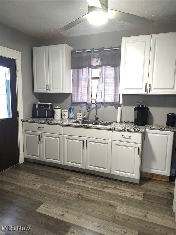 kitchen featuring dark hardwood / wood-style floors, sink, white cabinets, stone counters, and ceiling fan