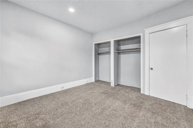 unfurnished bedroom with two closets, a textured ceiling, and carpet floors