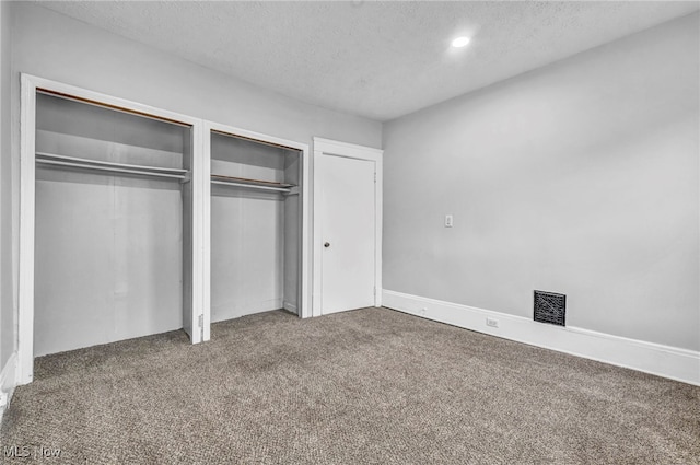 unfurnished bedroom featuring two closets, a textured ceiling, and carpet flooring