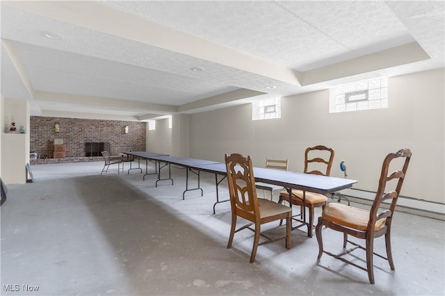 dining room featuring concrete flooring, a textured ceiling, a brick fireplace, and a baseboard heating unit