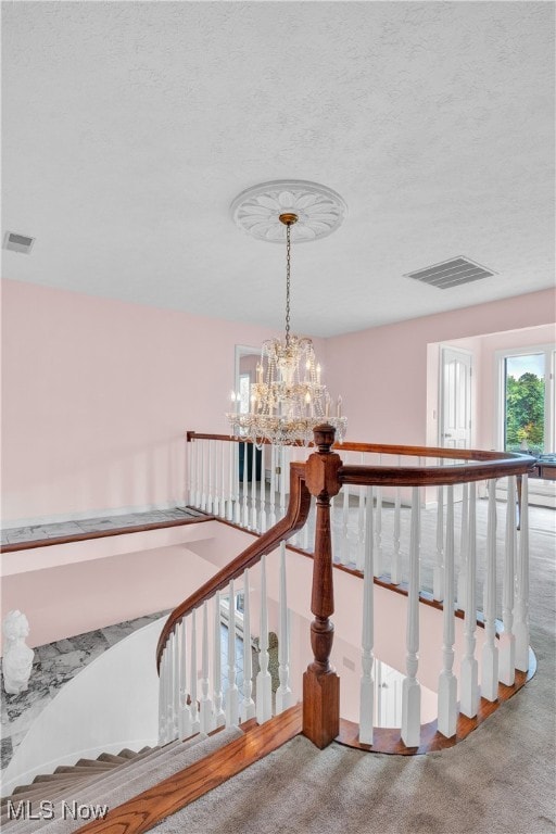 stairway featuring a chandelier, a textured ceiling, and carpet flooring