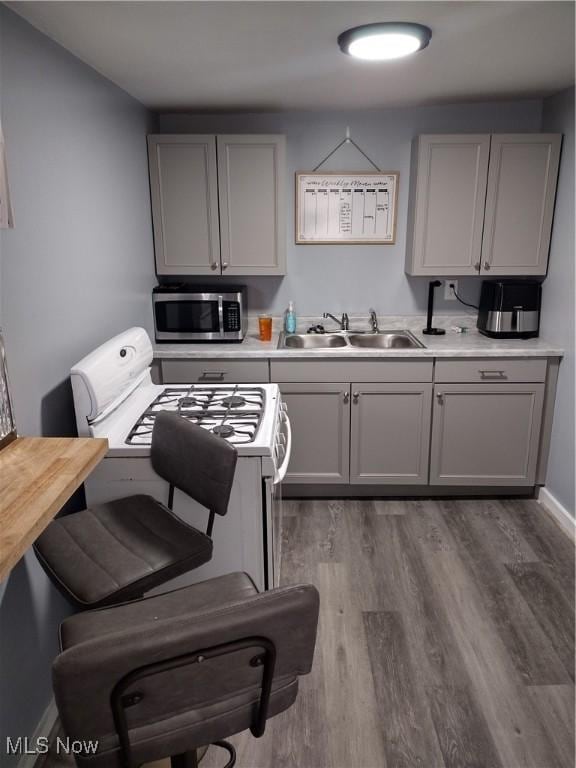 kitchen featuring stainless steel microwave, gray cabinetry, a sink, wood finished floors, and white range with gas stovetop