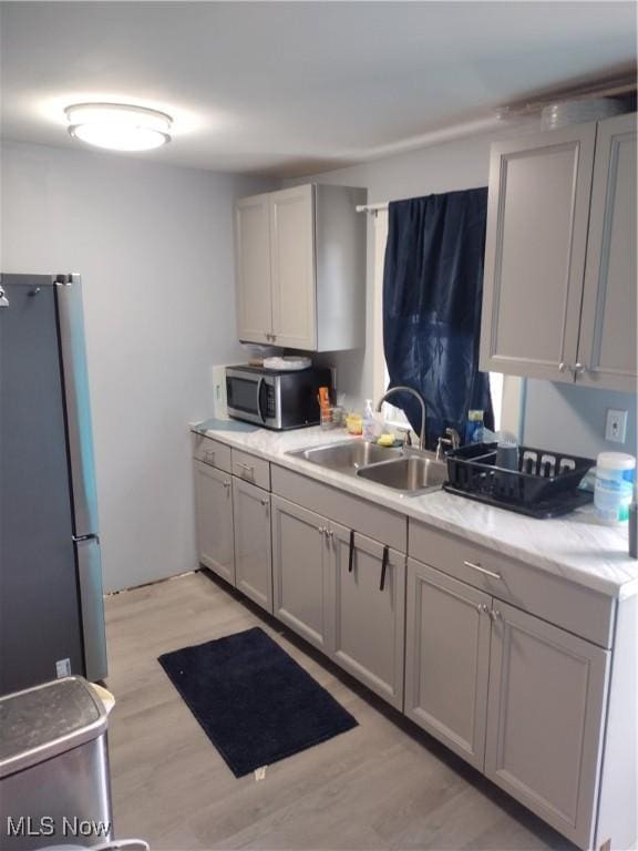 kitchen with appliances with stainless steel finishes, light wood-style floors, gray cabinets, and a sink