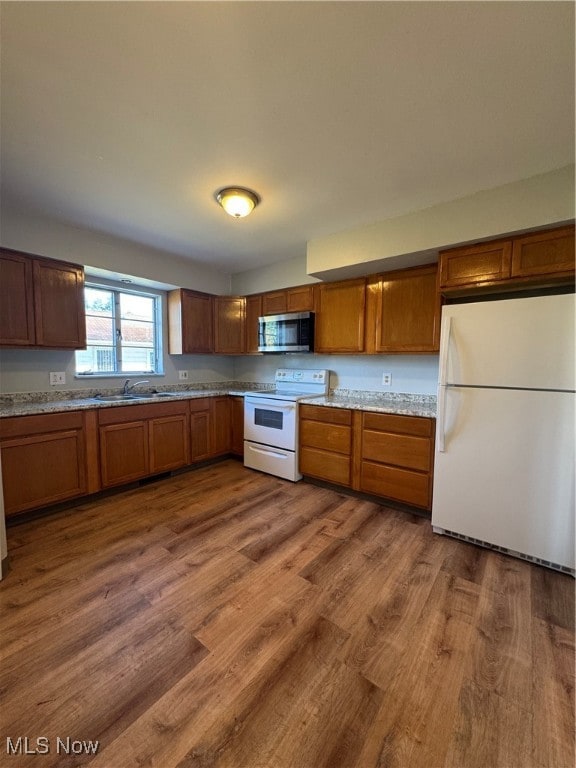 kitchen featuring light stone counters, sink, white appliances, and hardwood / wood-style flooring