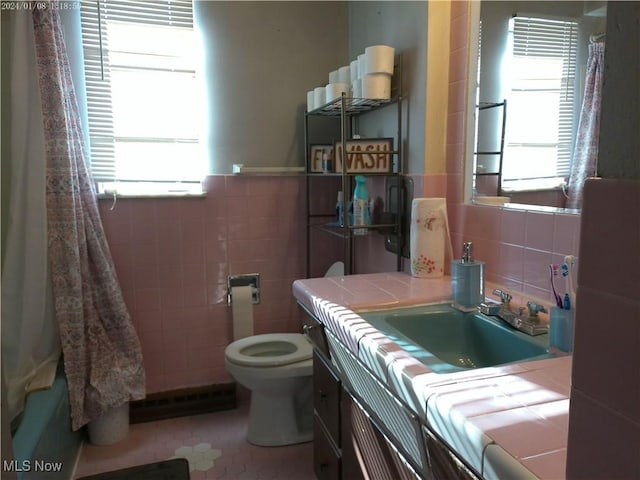 bathroom with toilet, a healthy amount of sunlight, tile walls, and vanity