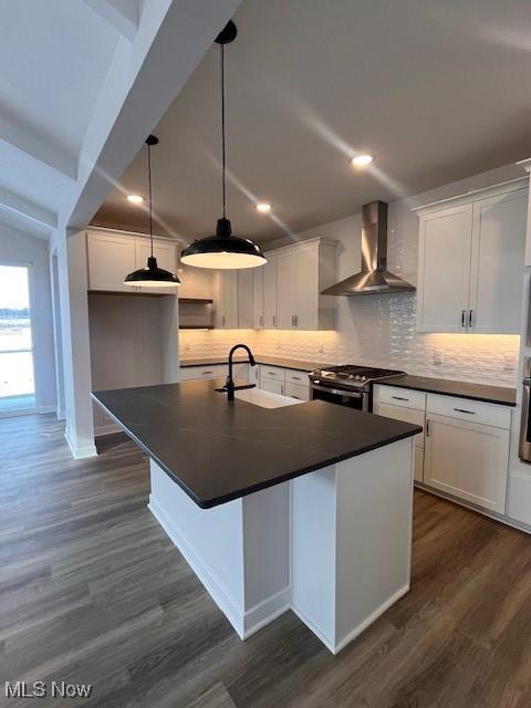 kitchen featuring white cabinets, a center island with sink, wall chimney exhaust hood, and stainless steel range with gas stovetop