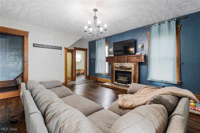 living room with a stone fireplace, a notable chandelier, dark hardwood / wood-style floors, and a textured ceiling