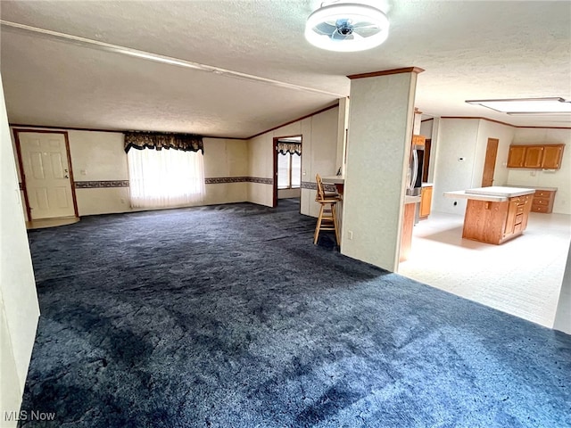 unfurnished living room featuring a textured ceiling, ornamental molding, and dark colored carpet