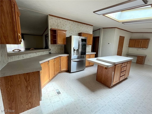 kitchen featuring a center island, stainless steel refrigerator with ice dispenser, kitchen peninsula, a skylight, and crown molding