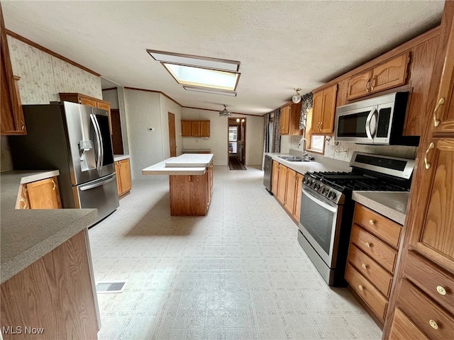 kitchen with a textured ceiling, a center island, sink, stainless steel appliances, and crown molding