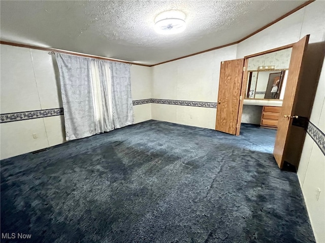 carpeted empty room with a textured ceiling, crown molding, and built in desk