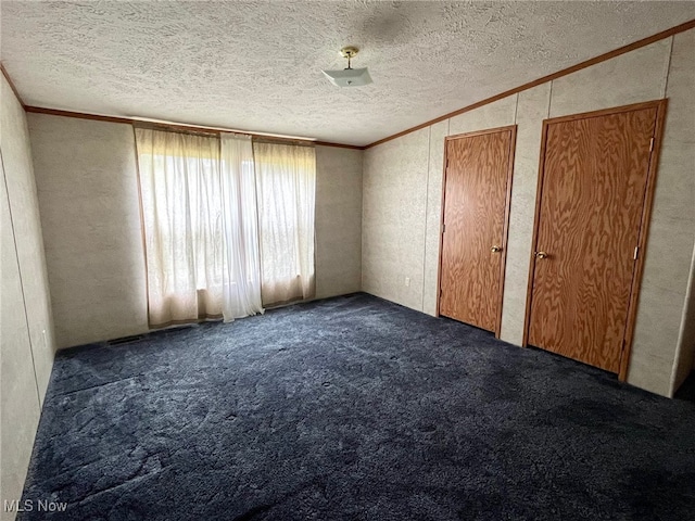 unfurnished bedroom featuring dark colored carpet, multiple closets, a textured ceiling, and crown molding