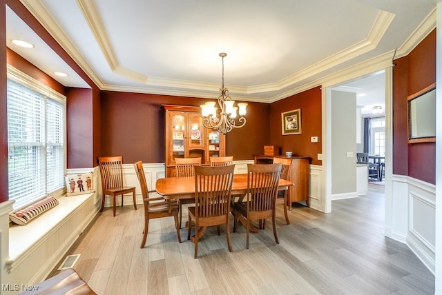 dining room featuring an inviting chandelier, a raised ceiling, crown molding, and light hardwood / wood-style floors