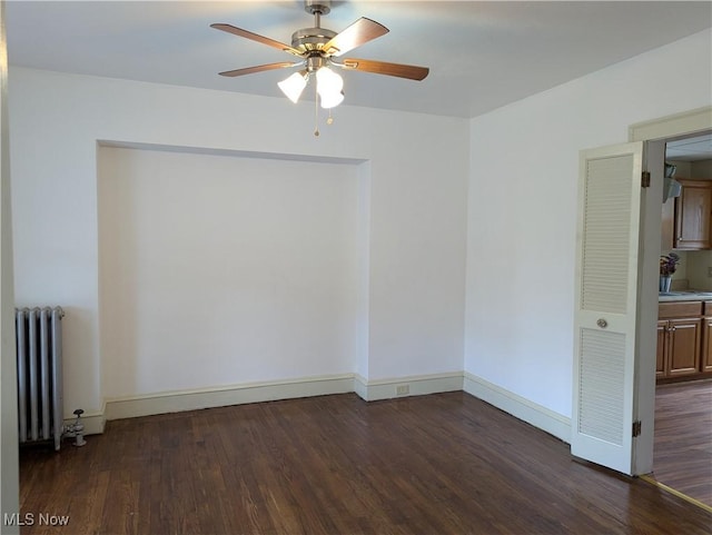 spare room featuring baseboards, wood finished floors, a ceiling fan, and radiator