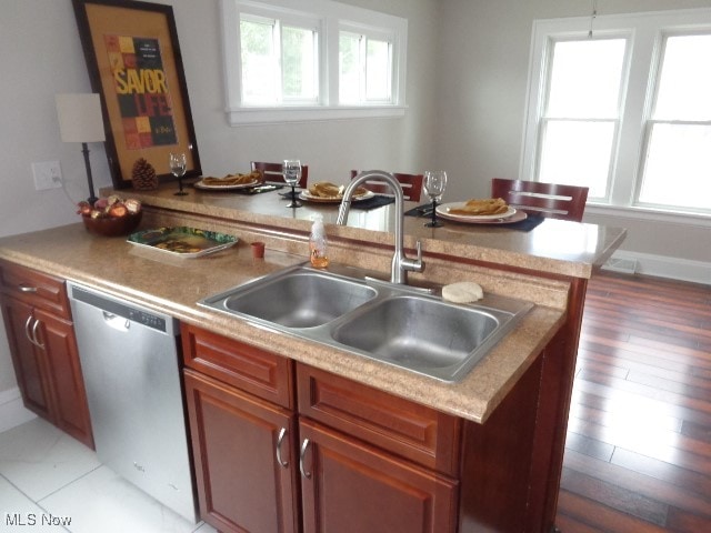 kitchen featuring a kitchen island with sink, sink, hanging light fixtures, light hardwood / wood-style flooring, and stainless steel dishwasher