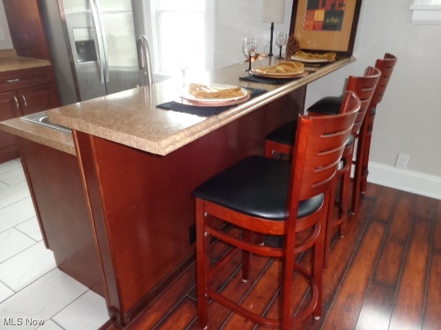 bar with stainless steel fridge and dark tile patterned flooring