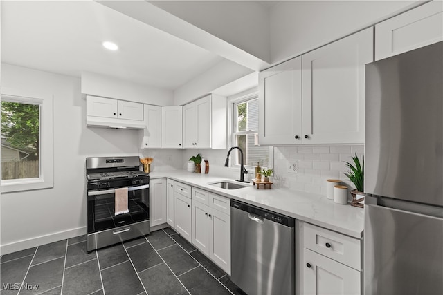 kitchen featuring appliances with stainless steel finishes, decorative backsplash, white cabinetry, dark tile patterned floors, and sink