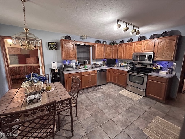 kitchen with appliances with stainless steel finishes, tile countertops, a chandelier, pendant lighting, and sink