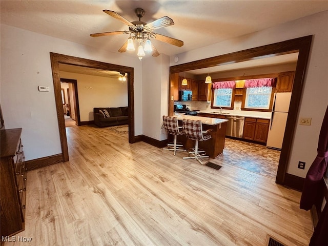 kitchen with a kitchen breakfast bar, hanging light fixtures, black appliances, and light wood-type flooring