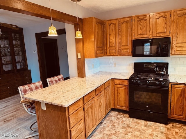 kitchen featuring black appliances, a kitchen bar, kitchen peninsula, and light hardwood / wood-style flooring