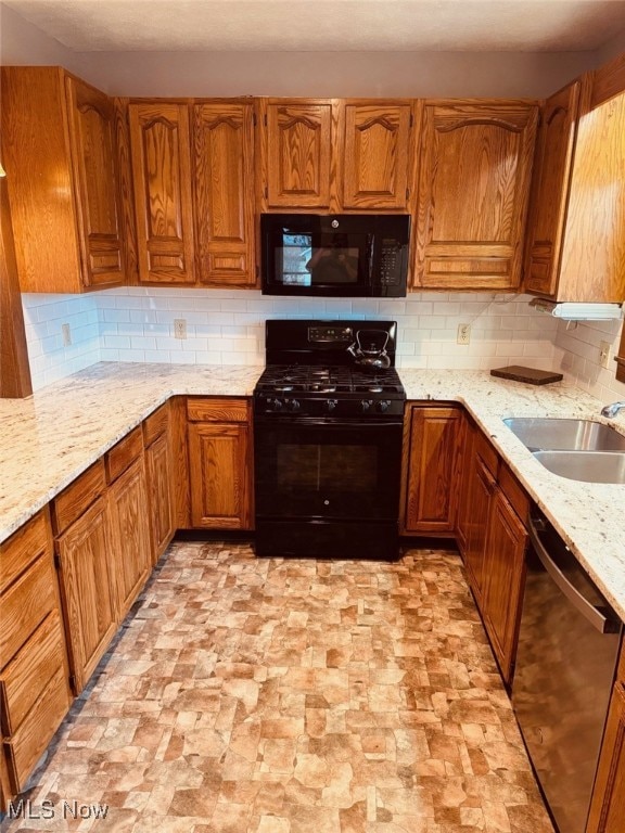 kitchen featuring decorative backsplash, sink, light stone countertops, and black appliances