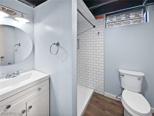 bathroom featuring wood-type flooring, tiled shower, vanity, and toilet