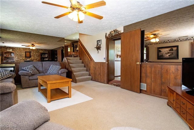 living room with ceiling fan, a textured ceiling, wood walls, and light carpet