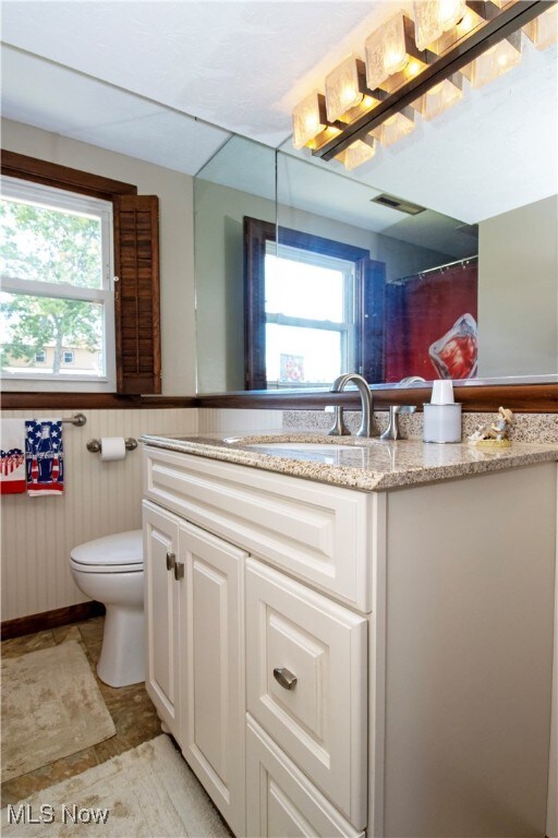 bathroom with a shower with shower curtain, vanity, toilet, and a wealth of natural light