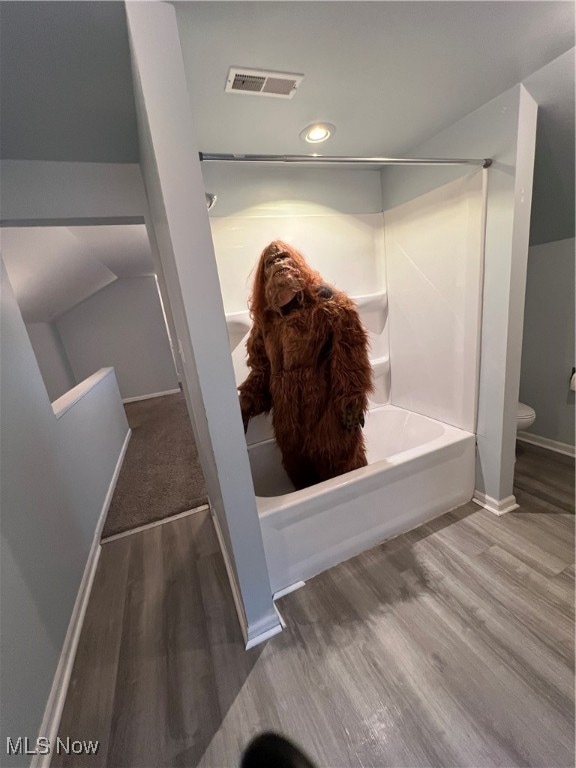 bathroom with shower / bathing tub combination, hardwood / wood-style floors, and toilet