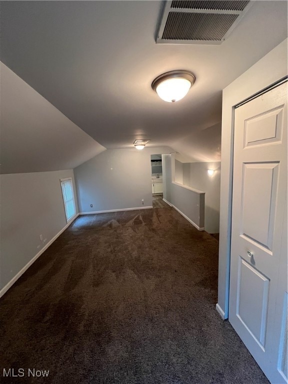 additional living space with dark colored carpet and vaulted ceiling