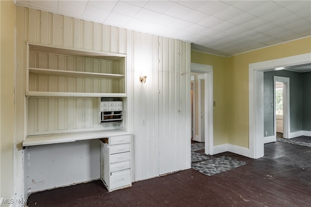 unfurnished office featuring built in desk, dark hardwood / wood-style floors, and wood walls