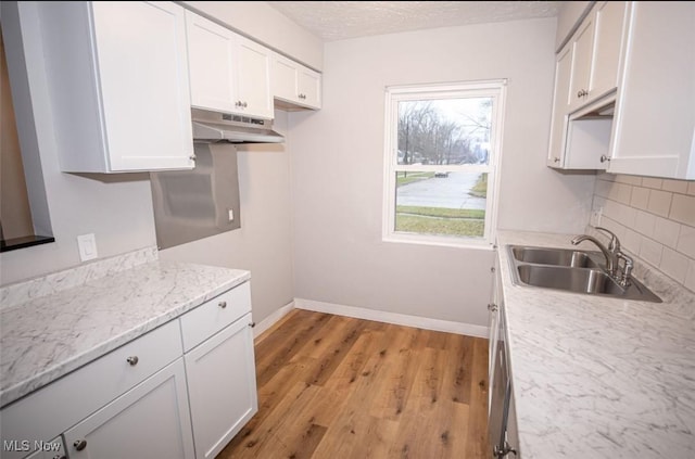 kitchen featuring sink, light stone counters, light hardwood / wood-style flooring, white cabinets, and backsplash