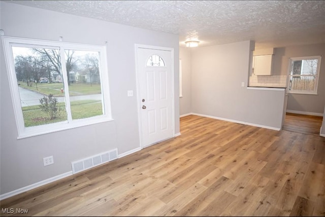 foyer entrance with a wealth of natural light, a textured ceiling, and light wood-type flooring