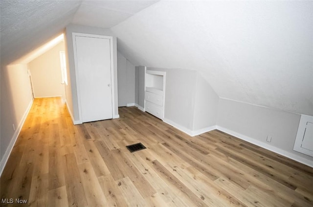 additional living space with lofted ceiling, light hardwood / wood-style floors, and a textured ceiling