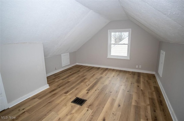 additional living space with lofted ceiling, wood-type flooring, and a textured ceiling