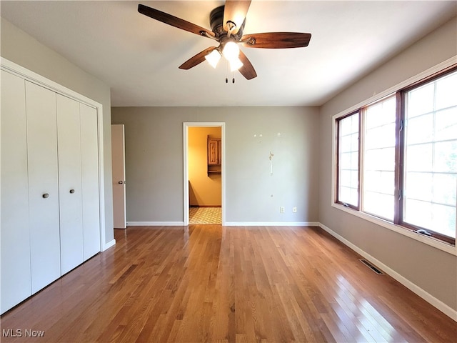 unfurnished bedroom featuring ceiling fan, ensuite bathroom, a closet, and light hardwood / wood-style floors