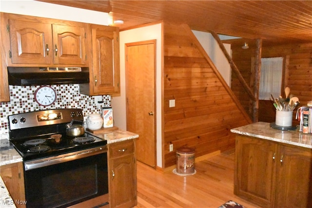 kitchen featuring stainless steel electric stove, backsplash, wood walls, light stone countertops, and light wood-type flooring