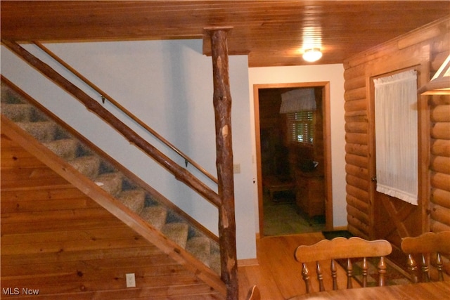 stairs featuring wooden ceiling, hardwood / wood-style floors, and rustic walls