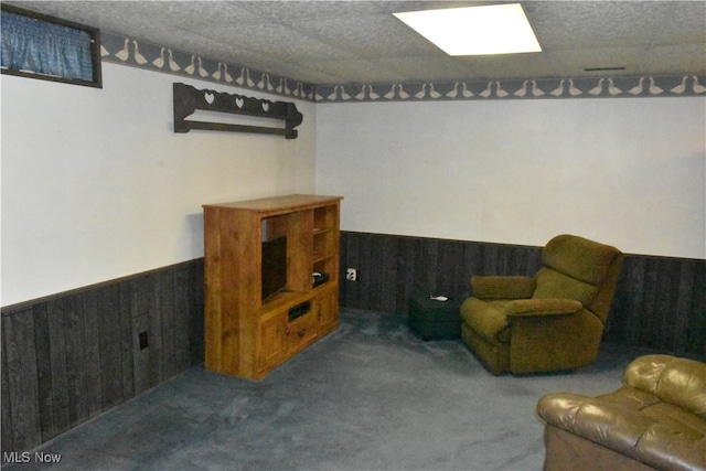 living area with a textured ceiling, carpet flooring, and wood walls