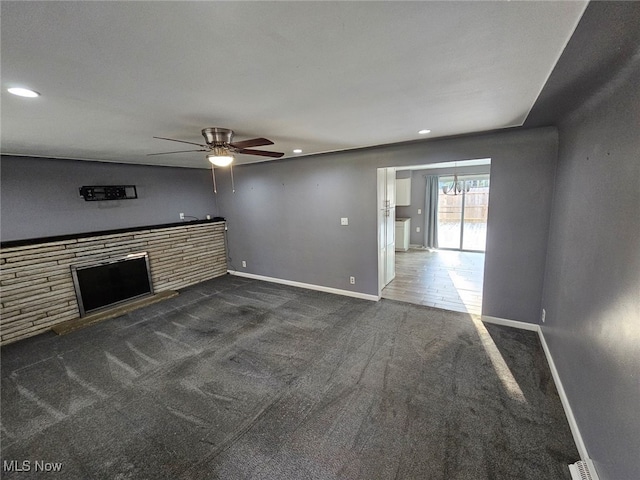 unfurnished living room with ceiling fan, a fireplace, and dark carpet