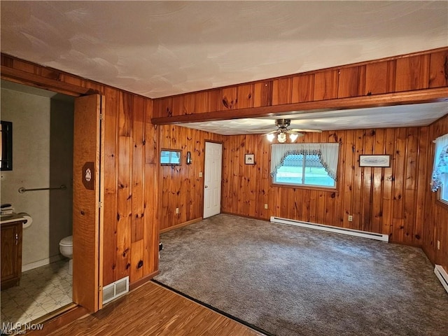 interior space with ceiling fan, wooden walls, baseboard heating, and hardwood / wood-style floors