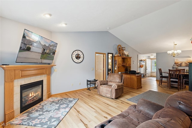 living room with an inviting chandelier, vaulted ceiling, a tiled fireplace, and light hardwood / wood-style flooring