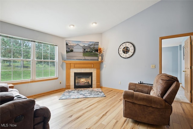 living room featuring lofted ceiling, a tile fireplace, and light hardwood / wood-style flooring