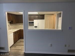 kitchen featuring dark brown cabinets, light hardwood / wood-style flooring, tasteful backsplash, and white appliances