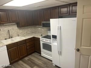 kitchen featuring decorative backsplash, white appliances, hardwood / wood-style flooring, dark brown cabinetry, and sink