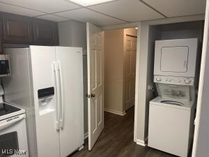 kitchen featuring dark hardwood / wood-style flooring, white appliances, a paneled ceiling, and stacked washing maching and dryer