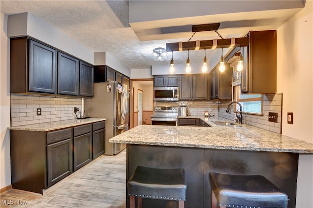 kitchen featuring appliances with stainless steel finishes, hanging light fixtures, kitchen peninsula, and sink