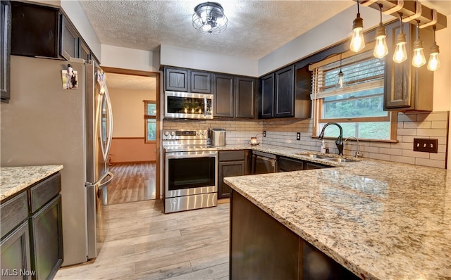 kitchen with decorative light fixtures, stainless steel appliances, light wood-type flooring, and sink